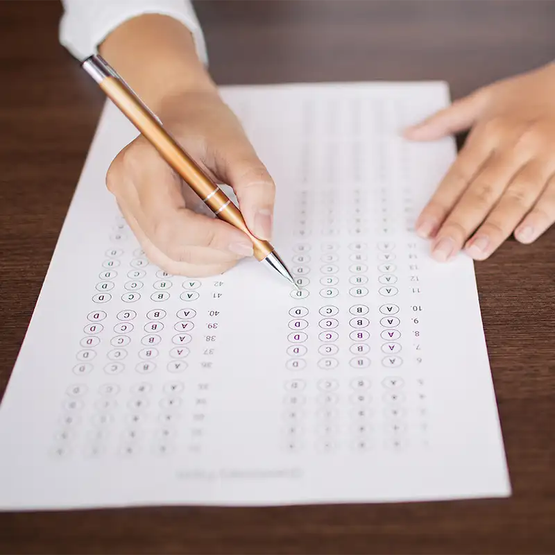 Close-up of female hand holding pen and marking answers in questionnaire form. Student doing examination test